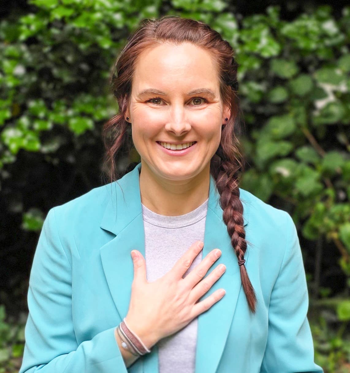Annika Brüggemann lächelt in die Kamera, eine Hand auf dem Herzen, vor grünem Laub