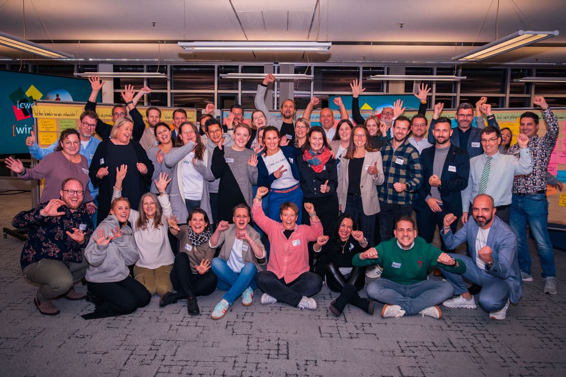 Große Gruppe von Workshopteilnehmenden beim gemeinsamen Gruppenfoto mit erhobenen Armen