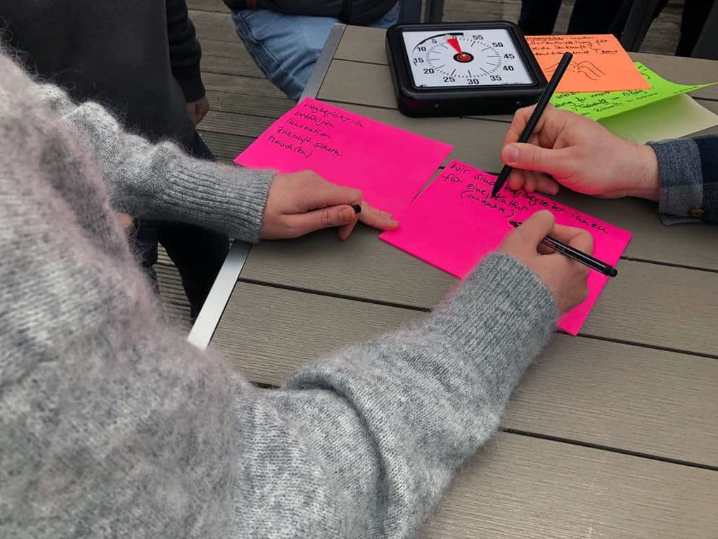 Zwei Personen beschriften am Tisch pinkfarbene Moderationskarten