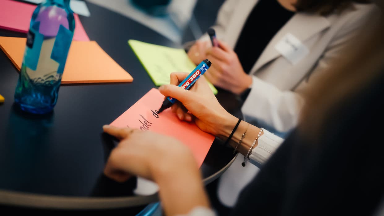 Hand beschriftet während eines Workshops eine Moderationskarte