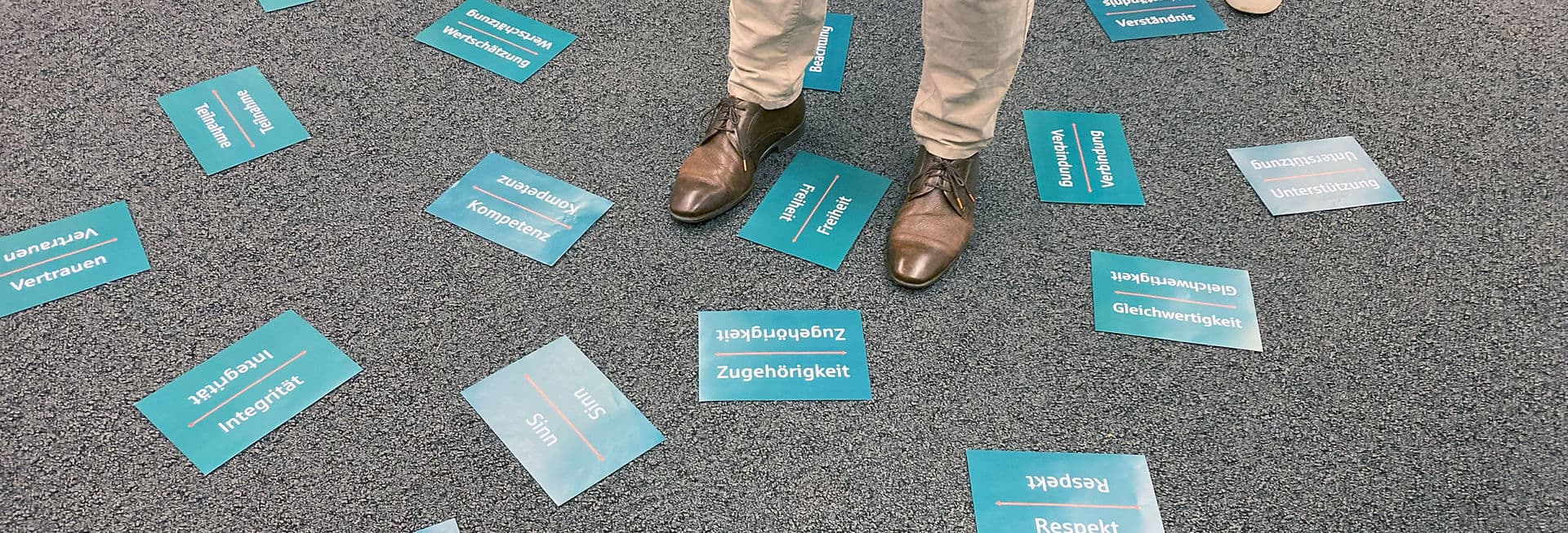 Moderationskarten mit Begriffen wie Vertrauen, Freiheit und Zugehörigkeit liegen auf dem Boden eines Workshopraums, dazwischen steht eine Person